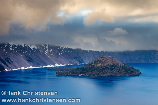 The orange hues of sunset light the overcast sky over Wizard Island, Crater Lake National Park, Oregon