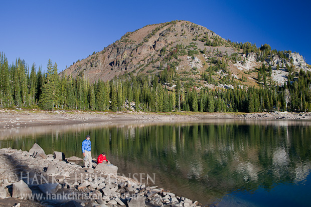 Two backpackers pump water from Crater Lake in the early morning as the surrounding hillside reflects off the lake's surface, Eagle Cap Wilderness, Oregon