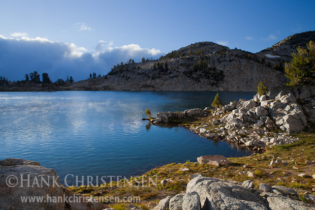 Sun peaks over a cloud bank, touching the surface of Glacier Lake, Eagle Cap Wilderness, Oregon