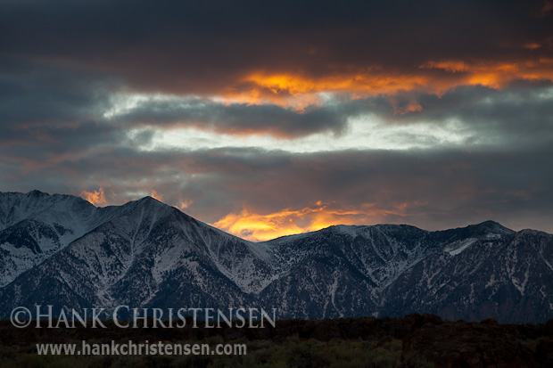 The sun plays dramatically across storm clouds as it sets behind the eastern Sierra range