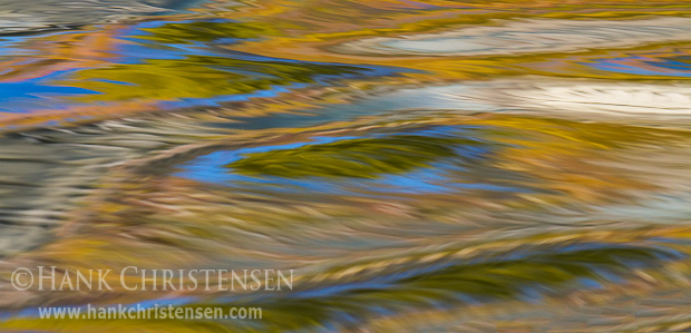 Fall colors are reflected in the surface of moving water ripples. The ripples turn simple reflections into endless patterns.