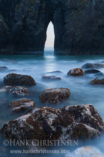 The tide washes through a sea arch, allowing a view to the ocean beyond, Harris State Beach