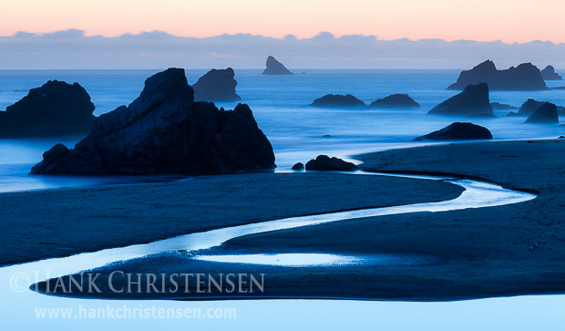 The sun sets behind a bank of offshore clouds, silhouetting the sea stacks at Harris State Beach, Oregon