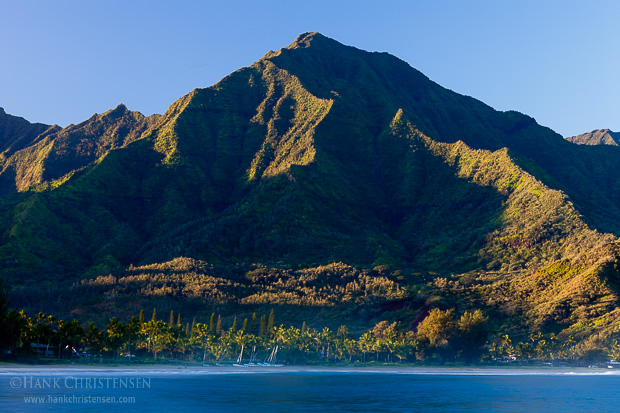 Green mountains covered with waterfalls rise from the shores of Hanalei Bay, catching the first rays of sunlight, Kauaii