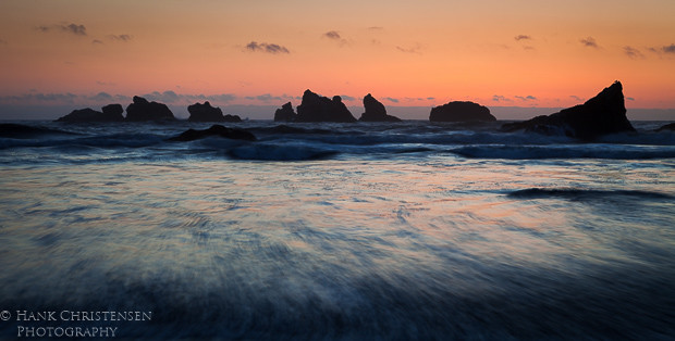 The sun sets behind the western horizon, casting the offshore sea stacks into shadow, Bandon, Oregon