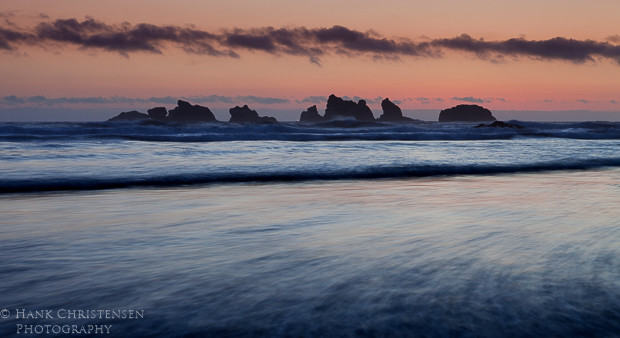 The sun sets behind the western horizon, casting the offshore sea stacks into shadow, Bandon, Oregon