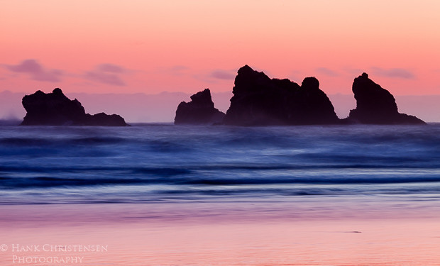 The sun sets behind the western horizon, casting the offshore sea stacks into shadow, Bandon, Oregon