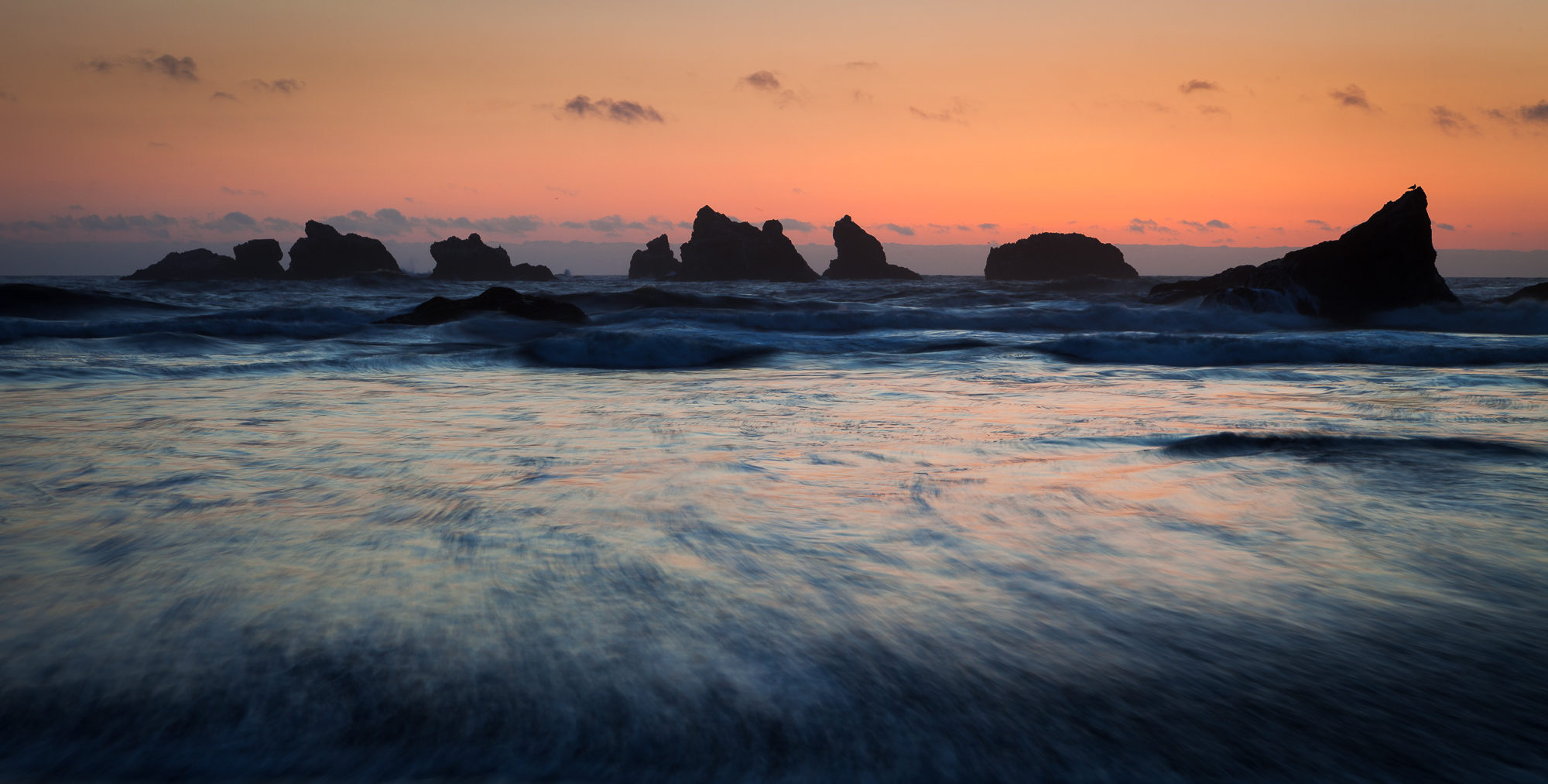 The sun sets behind the western horizon, casting the offshore sea stacks into shadow, Bandon, Oregon