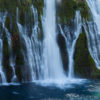 Burney Falls drops across a wide cliff into a pool below, creating a tree-lined grotto.