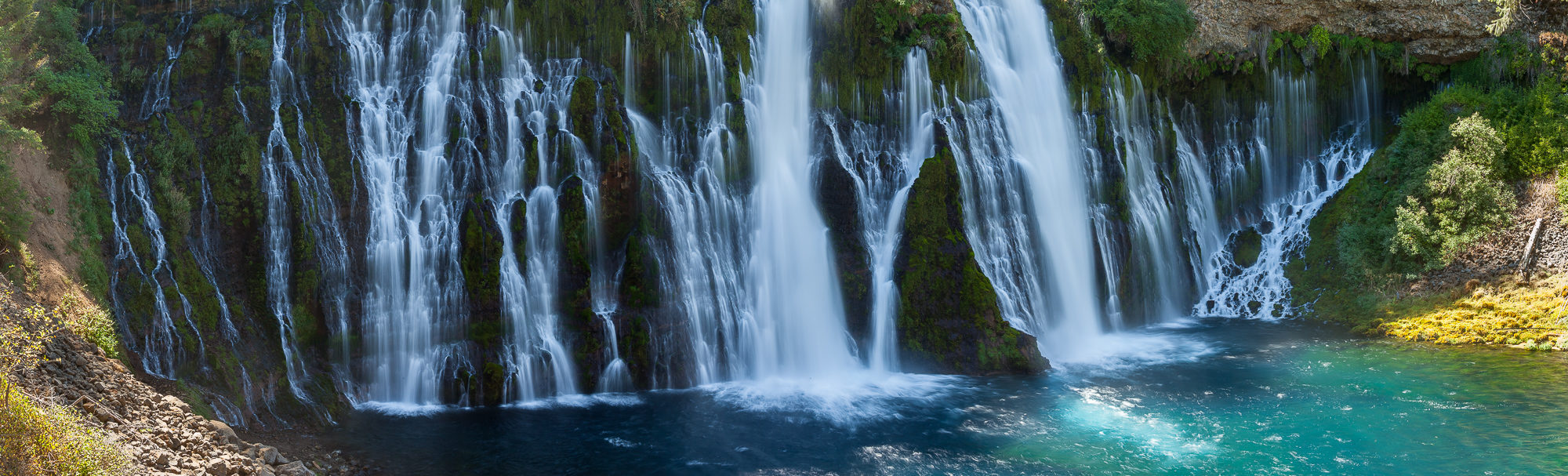 Burney Falls drops across a wide cliff into a pool below, creating a tree-lined grotto.