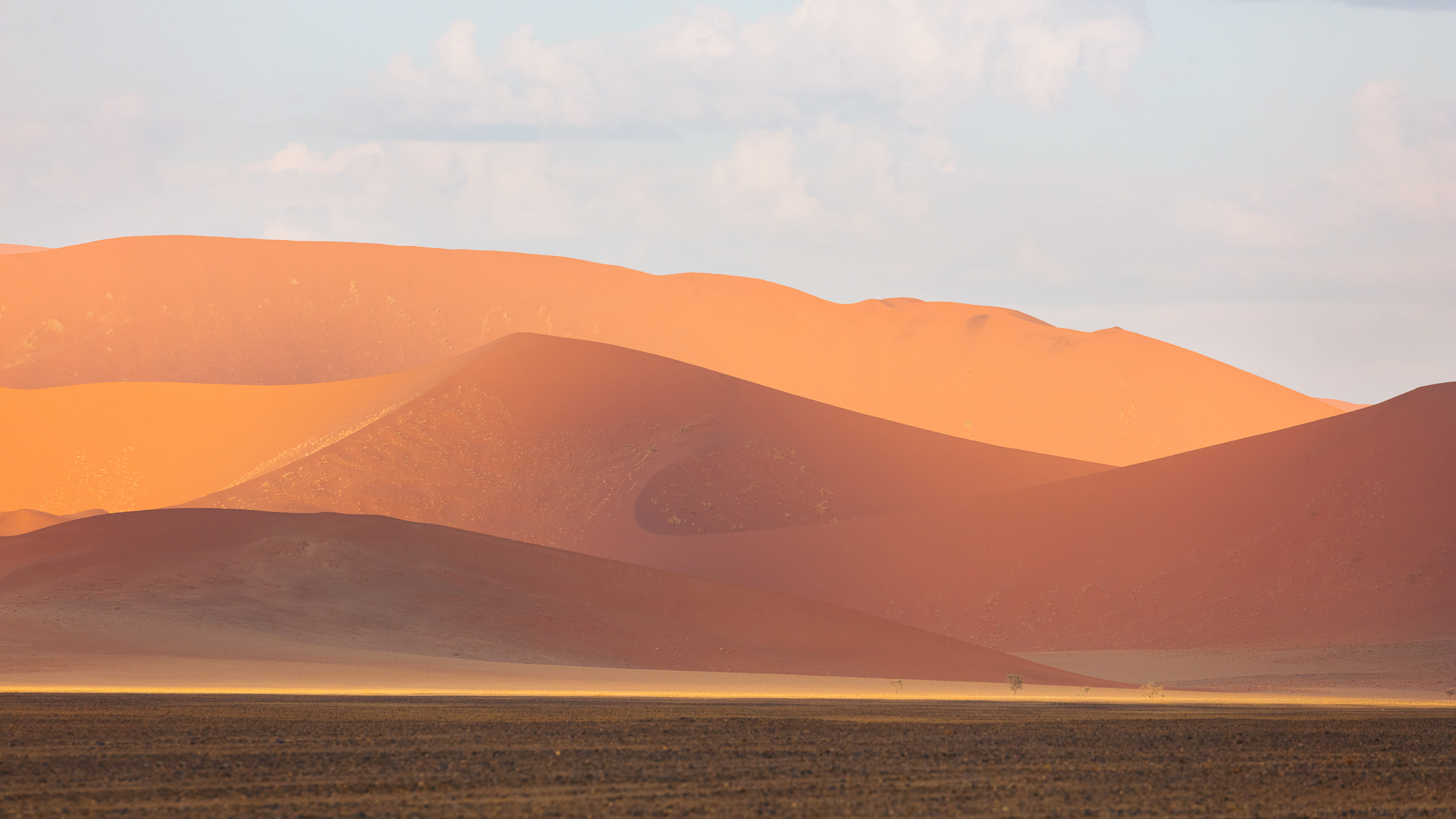 The giant sand dunes of Namibia turn many shades of red and orange under shifting clouds, Namib-Naukluft National Park, Namibia.